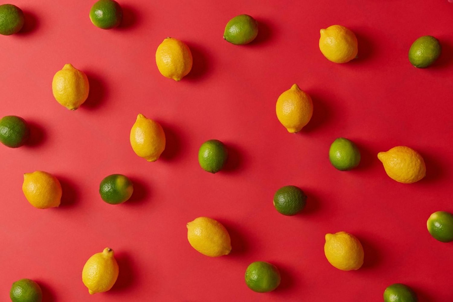 Yellow lemons and green limes scattered on a red background, representing citrus vape flavour appeal